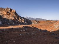 a red dirt road leading to a desert mountain with rocks and mountains in the background