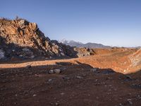 a red dirt road leading to a desert mountain with rocks and mountains in the background