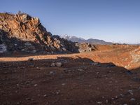 a red dirt road leading to a desert mountain with rocks and mountains in the background