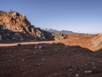 a red dirt road leading to a desert mountain with rocks and mountains in the background