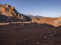 a red dirt road leading to a desert mountain with rocks and mountains in the background