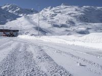 a truck drives along the snow - covered road through mountains under a clear blue sky