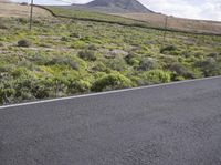 an asphalt road with a mountain in the distance with shrubs and a dirt area behind it