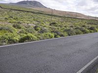 an asphalt road with a mountain in the distance with shrubs and a dirt area behind it