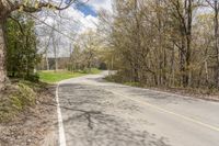 a empty road in the middle of some trees and trees around it, leading toward a street where there are a few vehicles