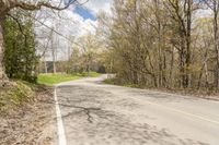 a empty road in the middle of some trees and trees around it, leading toward a street where there are a few vehicles
