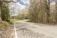 a empty road in the middle of some trees and trees around it, leading toward a street where there are a few vehicles