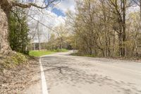 a empty road in the middle of some trees and trees around it, leading toward a street where there are a few vehicles