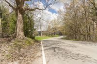 a empty road in the middle of some trees and trees around it, leading toward a street where there are a few vehicles