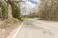 a empty road in the middle of some trees and trees around it, leading toward a street where there are a few vehicles