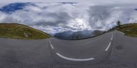 a curved road going up and down in a mountain scenery, with lots of cloud over it