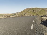 a road with rocks on both sides and green hills in the back ground and blue sky with few clouds