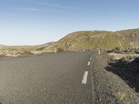 a road with rocks on both sides and green hills in the back ground and blue sky with few clouds