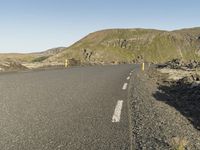 a road with rocks on both sides and green hills in the back ground and blue sky with few clouds