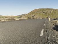 a road with rocks on both sides and green hills in the back ground and blue sky with few clouds