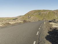 a road with rocks on both sides and green hills in the back ground and blue sky with few clouds