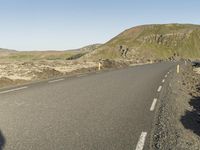 a road with rocks on both sides and green hills in the back ground and blue sky with few clouds