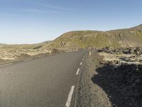 a road with rocks on both sides and green hills in the back ground and blue sky with few clouds