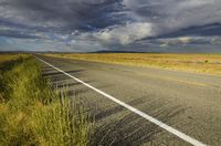 a single empty road on the prairie with dark clouds above it with a yellow stripe in between two rows