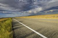 a single empty road on the prairie with dark clouds above it with a yellow stripe in between two rows