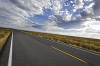 a road running along the side of a prairie with clouds and a blue sky above the road