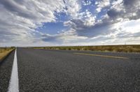 a road running along the side of a prairie with clouds and a blue sky above the road