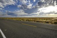 a road running along the side of a prairie with clouds and a blue sky above the road