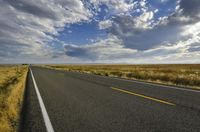 a road running along the side of a prairie with clouds and a blue sky above the road