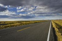 a road running along the side of a prairie with clouds and a blue sky above the road