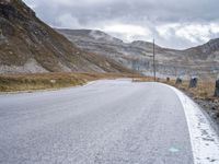 a road in the mountains with two cattle near it and one cow grazing in the distance