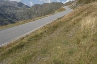 a large motorcycle is driving down the winding country road through the mountains along the grassy hillside, in front of mountains