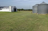 two large grain bins sit in the center of a field, surrounded by silos