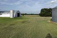 two large grain bins sit in the center of a field, surrounded by silos