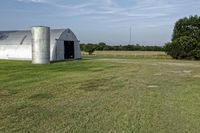 two large grain bins sit in the center of a field, surrounded by silos