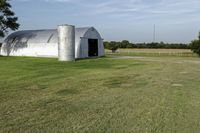 two large grain bins sit in the center of a field, surrounded by silos