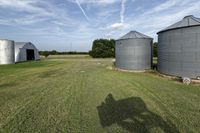 two large grain bins sit in the center of a field, surrounded by silos