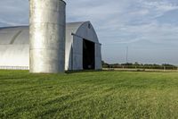 two large grain bins sit in the center of a field, surrounded by silos