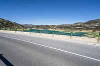 green barrier on paved road leading to lake view on sunny day, with mountain in background