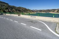 green barrier on paved road leading to lake view on sunny day, with mountain in background