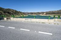 green barrier on paved road leading to lake view on sunny day, with mountain in background