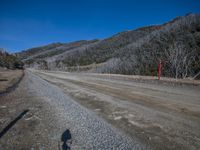 a road with a small hill in the background, and two bicycle riders shadow on the ground