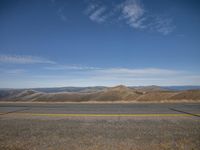 a large expanse of dry grass, hills and a road leading to the horizon on a sunny day