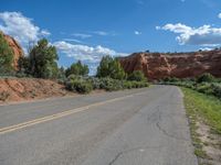 a desert road in the desert with mountains behind it and green plants below the road