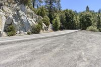 the empty road is winding through the rocky area near the tree line on the left side