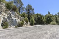 the empty road is winding through the rocky area near the tree line on the left side