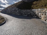 a road with stone blocks leading up to a hill next to a green grass hill