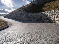 a road with stone blocks leading up to a hill next to a green grass hill