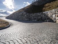 a road with stone blocks leading up to a hill next to a green grass hill