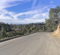 a paved road winding up to the top of a hill with trees on both sides and mountains beyond