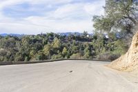 a paved road winding up to the top of a hill with trees on both sides and mountains beyond